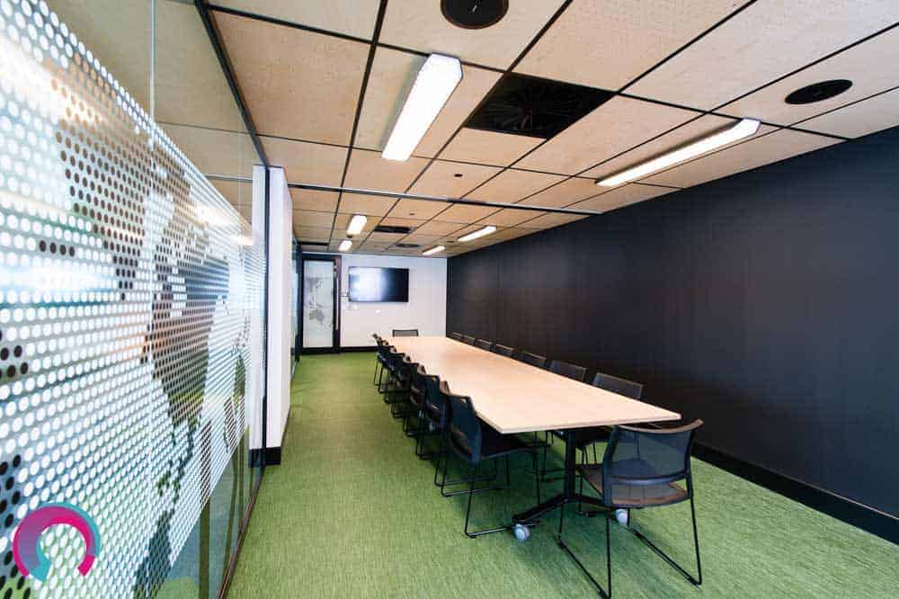 Meeting room showing long timber desk with black chairs and green carpet, with glass walls on one side, showing map of world on the glass. Black wall on opposite side - commercial office photography Brisbane
