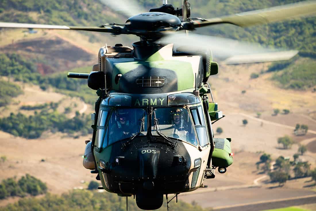 Close up of an Australian Army MRH Taipan Helicopter in the air, photographed from above, showing both pilot's faces, shot from the ramp of another MRH